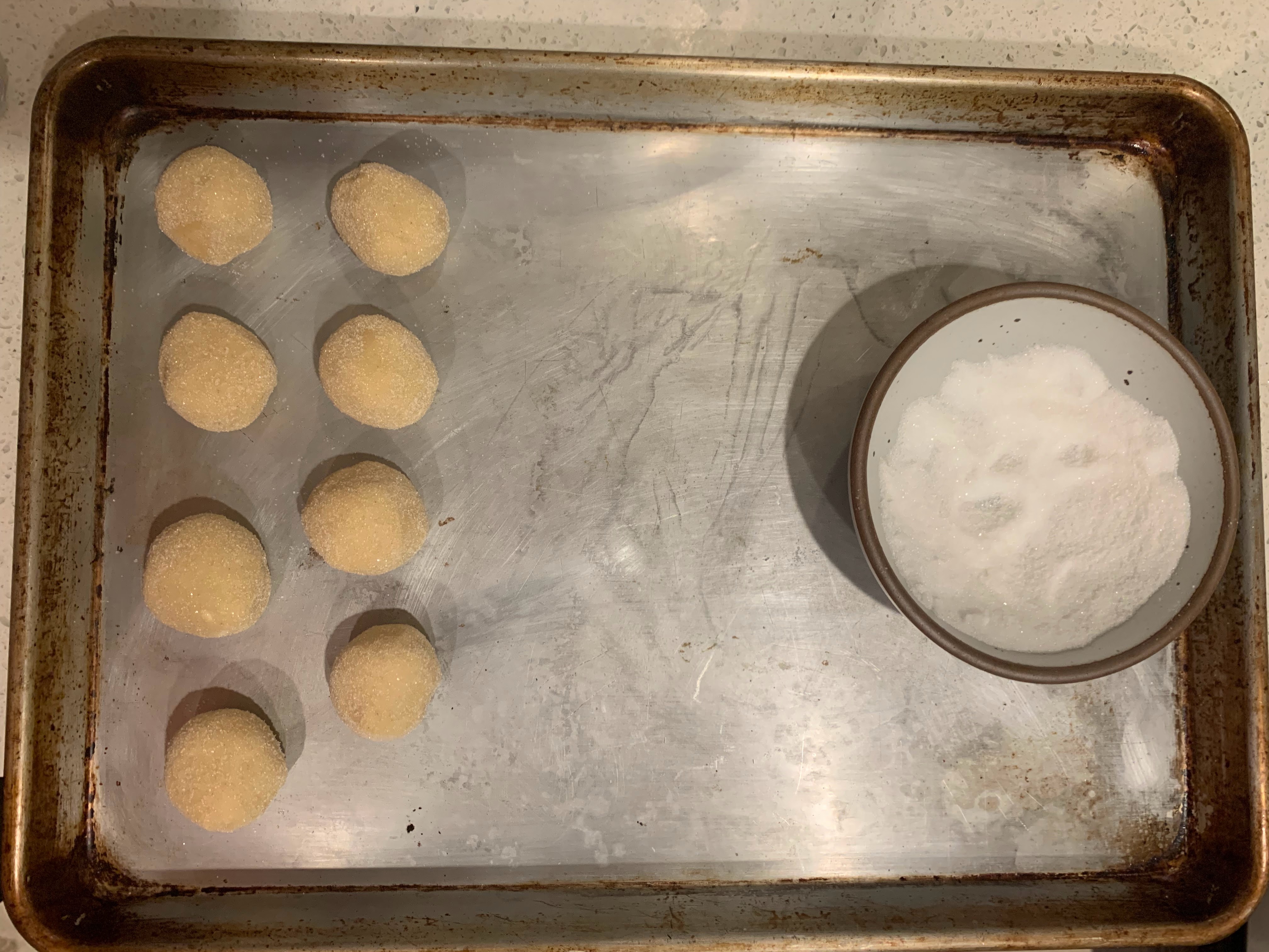 Dough balls coated in sugar on baking sheet